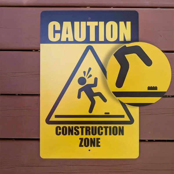 Yellow Caution Construction Zone Metal Sign, front view magnified, featuring a figure stepping on a brick, by True North Bricks, available at Infinite Brick